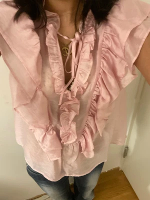 Rosa blus med volanger  - Jättesöt rosa blus som har volanger och går att knyta i mitten!❤️ Använd max två gånger och är glansigare i verkligheten!