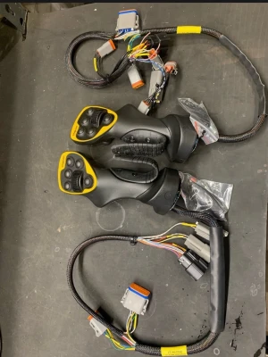 Svarta joystick-handkontroller med kablage - Säljer två svarta joystick-handkontroller med gula detaljer och tillhörande kablage. Handtagen har flera knappar och tumspakar, samt ergonomiskt grepp. Perfekt för simulatorer eller specialbyggda spelriggar. Materialet är plast och kablarna är skyddade med flätad hylsa.