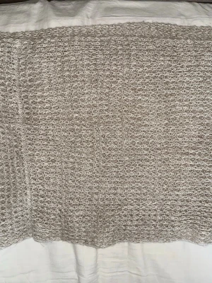 Beige stickad tubhalsduk - Säljer en beige stickad tubhalsduk i mjukt och luftigt garn. Halsduken har ett grovt, öppet mönster som ger en avslappnad och trendig look. Perfekt att slänga på sig för extra värme och stil under kyliga dagar.