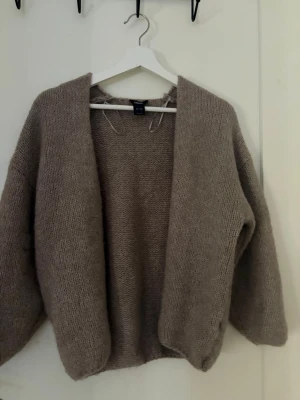 Beige stickad kofta - Mysig beige stickad kofta med öppen front och avslappnad passform. Koftan har långa ärmar och är gjord i ett mjukt, fluffigt material som passar perfekt för kyliga dagar. Enkel och stilren design som är lätt att matcha med olika outfits.