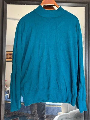 Turkos stickad polotröja - Snygg turkos stickad polotröja med lång ärm och ribbade muddar vid ärmslut och nederkant. Perfekt för dig som gillar en enkel men stilren look. Tröjan har en hög krage och är tillverkad i ett mjukt material.