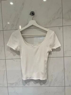 Vit ribbad topp med djup urringning - Säljer en vit ribbad topp med korta ärmar och djup, rund urringning i strl S/36. Toppen är figurnära och har en enkel, stilren design som passar till det mesta. Perfekt för dig som gillar en clean och fräsch look🤍✨