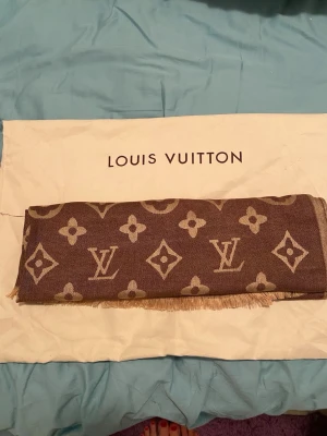 Brun Louis Vuitton halsduk - Säljer en brun halsduk från Louis Vuitton med det klassiska monogrammönstret i beige. Halsduken har fransade kanter och är tillverkad i ett mjukt tyg som känns lyxigt och stilrent. 65% Kashmir och resterande silke. Present från mitt otrogna ex så HEJDÅ säger jag till denna! 