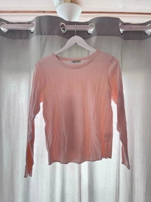 Ljusrosa ribbad långärmad pyjamas  - Säljer en ljusrosa långärmad topp med ribbad struktur och diskreta mönster i tyget. Toppen har rund halsringning och vågig kant nertill, perfekt för en trendig och avslappnad look. Tröjan i storlek M och byxor i storlek S