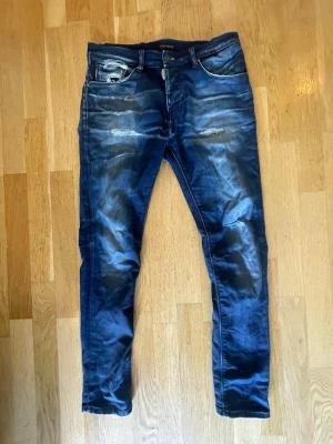 Antony Maraio jeans  - Säljer ett par blå skinny jeans med slitningar och distressed detaljer. Jeansen har fem fickor, knappgylf och tydliga slitningar på låren och knäna för en trendig look. Perfekta för dig som gillar en avslappnad och edgy stil.