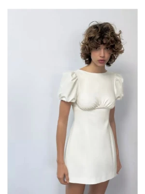Vit kort puffärmad klänning - Stilren vit kortklänning med puffärmar och markerad byst. Klänningen har en enkel, elegant design och är tillverkad i ett slätt material som ger en mjuk känsla. Perfekt för dig som gillar minimalistisk och trendig stil.
