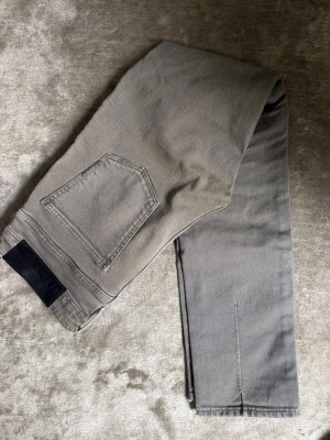 Neuw jeans - Säljer ett par grå skinny jeans från Neuw med slitningar på benen och klassisk femficksdesign. Jeansen har en smal passform och är tillverkade i ett stretchigt material för extra komfort. Perfekta för en avslappnad och trendig look.