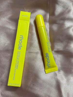 Rhode Peptide Lip Treatment Lemontini - Fräsch läppbalsam från Rhode i färgen Lemontini. Kommer i en klargul tub med matchande förpackning och blå text. Tuben rymmer 10 ml och har en smidig applikator. Perfekt för dig som vill ha återfuktade läppar med en hint av citrus.