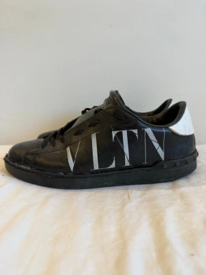 Valentino skor - Snygga svarta sneakers från Valentino med stor VLTN-logga på sidan och vit hälkappa. Skorna har klassisk låg profil, svarta skosnören och detaljer i läder. Perfekta för dig som vill ha en stilren men ändå statement sneaker. Skicket e sådär varav pris. 