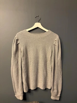 Ljusgrå stickad tröja  - Säljer en ljusgrå stickad tröja från SAMSA Collection. Tröjan har en ribbad struktur, rund halsringning och långa ärmar med lätt puff vid axlarna. 