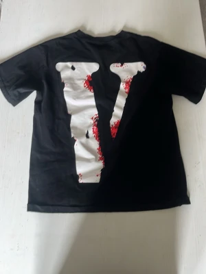Svart t-shirt med tryck och stor V - Cool svart t-shirt med stort vitt V på ryggen och tryck framtill med texten 'I ♥ TX' och en figur med motorsåg. T-shirten har korta ärmar och är i bomull. Perfekt för dig som gillar unika och edgy motiv.