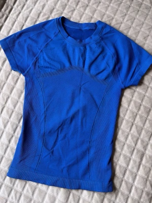 Blå sportig t-shirt med sömmar - Snygg blå sport-tshirt med korta ärmar och rund hals. Tröjan har markerade sömmar och ribbade detaljer vid ärmslut och nederkant. Tillverkad i ett stretchigt funktionsmaterial som andas, perfekt för träning eller aktivitet. Från SHEIN. 