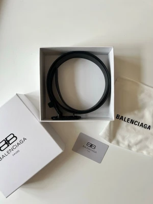 Svart Balenciaga bälte  - Snyggt svart skärp från Balenciaga i stilren design. Skärpet är tillverkat i skinn och har ett diskret BB-spänne framtill. Perfekt accessoar för att lyfta din outfit med en exklusiv touch. Kommer med låda, märkeskort, påse. Fråga också om ni vill ha bild på kvittot. (Bältet är 110cm)