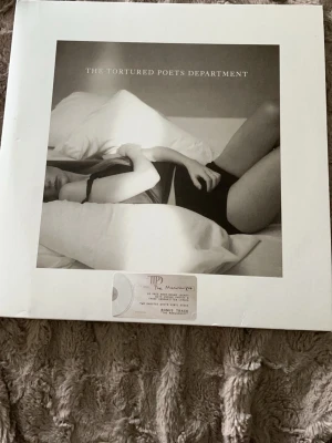 The Tortured Poets Department vinyl - Säljer en vinyl med titeln 'The Tortured Poets Department'. Omslaget är svartvitt med ett konstnärligt foto av Taylor swift som ligger på en säng. Baksidan har ett porträtt i samma stil och texten 'I love you, it's ruining my life'. Perfekt för dig som gillar poesi och snygg design.