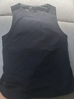 Svart ärmlös topp med knyt bak - Snygg svart ärmlös topp från SHEIN med rund halsringning och cool knytning i ryggen. Perfekt för dig som gillar stilrena plagg med en twist. Materialet känns mjukt och stretchigt, vilket gör den bekväm att bära hela dagen.