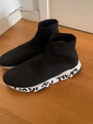 Svarta sock-sneakers med grafisk sula - Säljer ett par svarta sock-sneakers med stretchig ovandel i textil och högt skaft. Sulan är vit med svart grafiskt mönster som ger en unik look. Perfekta för dig som vill ha något trendigt och bekvämt till vardagslooken.