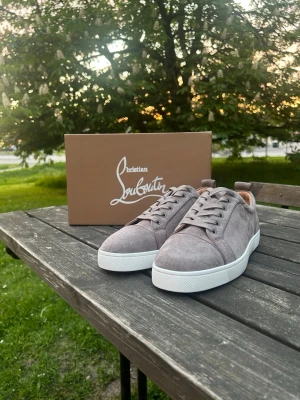 Gråa Loubs sneakers i mocka - Snygga gråa sneakers från loobs i mjuk mocka med klassisk röd sula och vita kanter. Lågt skaft och stilren design som passar perfekt till streetwear eller en mer uppklädd look. Skorna har matchande gråa skosnören och diskreta detaljer.