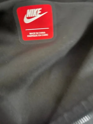 Nike tech fleece - Säljer en svart hoodie från Nike med klassisk logga. Hoodien har dragkedja och är tillverkad i mjukt material som passar perfekt för en chill och sportig stil. Storlek L. Perfekt för dig som gillar streetwear och vill ha något bekvämt och snyggt.