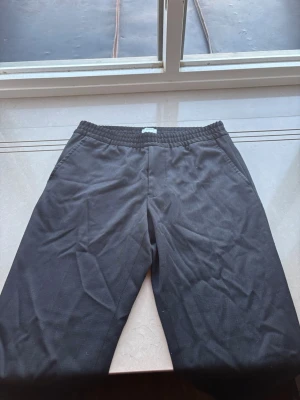 Svarta byxor från Filippa K - Svarta kostymbyxor från Filippa K med elastisk midja. Kan anvödnas som både kostymbyxor samt mer relaxed. Passar mig som är 185 