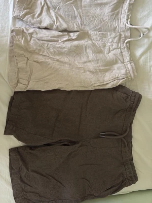Beige linneshorts med snörning - Snygga shorts i linne med avslappnad passform och snörning i midjan. Shortsen har sidofickor och elastisk midja för extra komfort. Perfekta för varma dagar och enkel att matcha med olika stilar. Ett par för 100 båda för 150