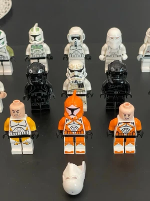 Samling LEGO Star Wars minifigurer - Säljer en samling LEGO Star Wars minifigurer med olika stormtroopers och piloter i vitt, svart, orange och gult. Figurerna har detaljerade dräkter och hjälmar, vissa med avtagbara huvuden och ansikten. Perfekt för dig som gillar Star Wars och LEGO!