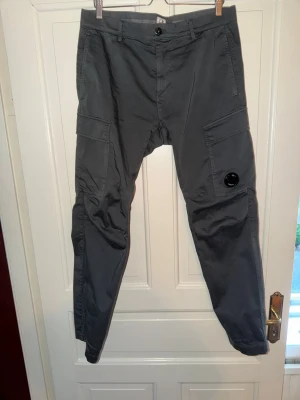 C.P. Company Cargo dark grey - C.P Company Cargobyxor inköpa på careofcarl för bara några månader sen. Lite impulsköp av mig och har använt dem ca 3ggr. Absolut nyskick. Skyddsfilmen på linsen sitter fortfarande kvar. Inga som helst skavanker eller fel. Säljes pga det ej var min stil.  Storlek 48IT. 98% bomull 2%elastan.                Nypris: SEK3000