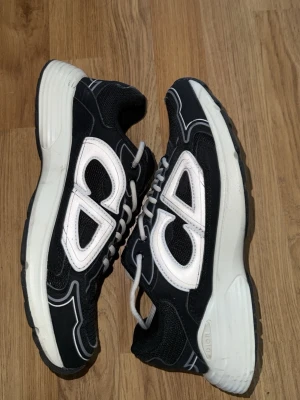 B30 - Snygga svarta sneakers med vit sula och stora vita detaljer på sidorna. Skorna har en sportig look med mesh och syntetmaterial, samt vita snören. Perfekta för dig som gillar streetwear och vill sticka ut med en unik design.