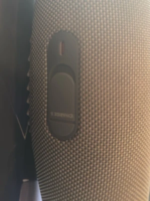 Grå JBL bärbar högtalare - Snygg grå bärbar högtalare från JBL med robust tygmaterial och rundad form. Perfekt för att ta med sig överallt tack vare den kompakta designen. Tydlig JBL-logga på sidan och praktiska knappar för enkel användning.