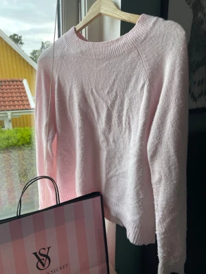 Ljusrosa stickad tröja - Mysig ljusrosa stickad tröja med rund halsringning och långa ärmar. Tröjan har ribbstickade muddar vid hals, ärmslut och nederkant. Perfekt för kyligare dagar och enkel att matcha med olika outfits.