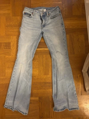 Ljusblå bootcut jeans - Säljer ett par ljusblå bootcut jeans med klassisk femficksmodell och normalhög midja. Jeansen har en lätt tvättad look och raka ben som går ut lite nedtill. Perfekta för en avslappnad och trendig stil.