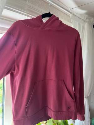 Vinröd hoodie med känguruficka - Säljer en vinröd hoodie med huva och känguruficka framtill. Hoodien har en enkel och clean design med ribbade muddar vid ärmslut och nederkant. Perfekt för dig som gillar en avslappnad och stilren look.