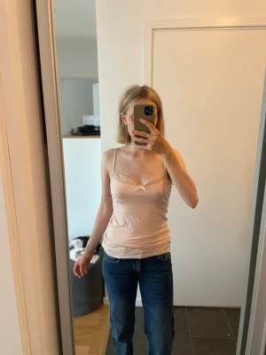 Pyjamaslinne med spetsdetaljer från Hunkemöller - Säljer ett ljust korall-färgat pyjamaslinne från Hunkemöller i storlek xs med tunna axelband och spetsdetaljer vid bysten. Toppen har en liten rosett framtill och är avslappnad i stilen. 50 kr!