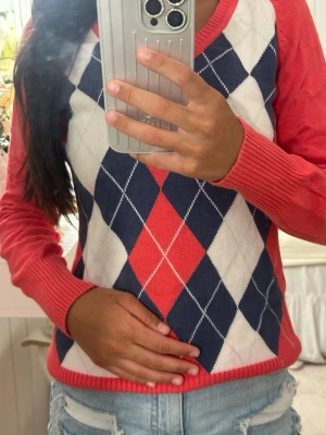 Argyle stickad tröja i rött och blått - (uppmärksamma de små fläckarna snälla) Stickad tröja från L.O.G.G. med klassiskt argylemönster i marinblått, rött och vitt. Tröjan har långa ärmar, ribbade muddar och V-ringning. Perfekt för dig som gillar preppy stil och vill ha något färgglatt i garderoben. 