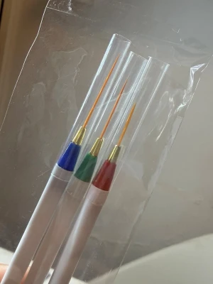 3-pack nail art penselset - Säljer ett set med tre nail art penslar med vita skaft och färgade detaljer i blått, grönt och rött. Penslarna har tunna, långa borst perfekta för detaljerad nageldesign. Varje pensel har ett genomskinligt skyddshölje och är numrerade 1, 2 och 3.