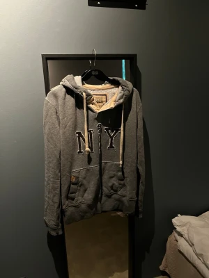 Grå hoodie med NY-tryck och huva - Säljer en grå hoodie från Better Rich med stort NY-tryck på bröstet. Hoodien har en stor ficka framtill, beigea dragsnören och mjuk insida. Perfekt för dig som gillar streetwear och vill ha en avslappnad stil.