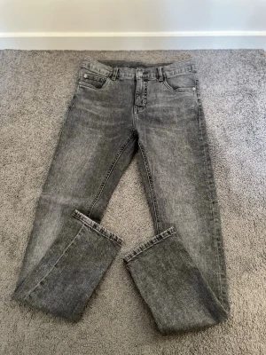 Grå tvättade raka jeans - Säljer ett par grå tvättade jeans med rak passform och klassisk femficksdesign. Jeansen har normal midja och är tillverkade i ett mjukt denimtyg. Perfekta för en avslappnad och trendig look.