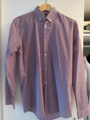 Rutig skjorta i rött, blått och vitt - Klassisk långärmad skjorta med smått rutigt mönster i rött, blått och vitt. Skjortan har knappar framtill och button-down krage. Perfekt till jeans eller chinos för en clean och stilren look. Medium
