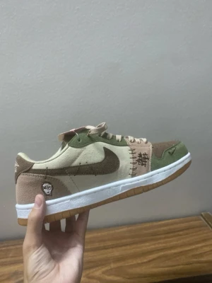 Beige och gröna sneakers med brodyr - Har storlek 38-45. Unika sneakers i beige, brunt och grönt med broderade detaljer och patchar. Skon har en vit sula med gummiyttersula och är tillverkad i mocka och textil. Swoosh-logga på sidan och broderad symbol på hälen. Perfekt för dig som gillar streetwear och snygga detaljer.
