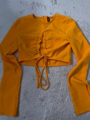 Orange croppad topp med snörning - Orange croppad topp med långa ärmar och snygg snörning framtill i storlek S. Toppen har rund halsringning och är tillverkad i ett mjukt material som känns skönt mot huden. Aldrig använd🩷