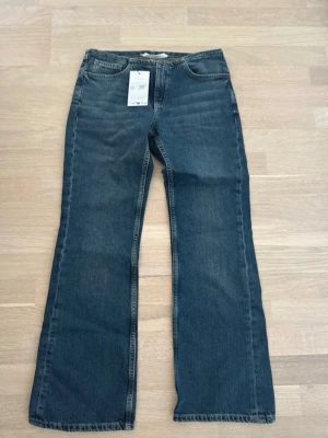 Blå bootcut jeans med fem fickor - Säljer ett par klassiska blå bootcut jeans med fem fickor och normal midja. Jeansen har en lätt tvättad look och raka ben som går ut något nedtill. Perfekta för dig som gillar en avslappnad men ändå trendig stil.
