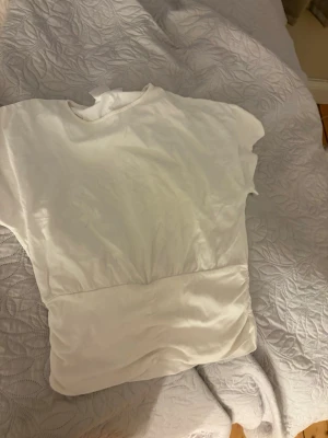 Vit t-shirt från Gina Tricot - En klassisk vit t-shirt från Gina Tricot i mjuk bomull. T-shirten har rund halsringning och korta ärmar, perfekt till alla typer av outfits. Enkel och stilren design som funkar till det mesta.