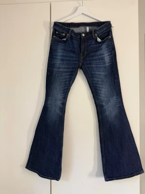 Mörkblå utsvängda jeans bootcut - Säljer ett par mörkblå bootcut jeans med utsvängda ben och klassisk femficksmodell. Jeansen har snygga slitningar framtill och är perfekta för dig som gillar en retroinspirerad look. Tillverkade i bomull för skön känsla.