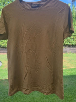 Brun t-shirt från Dressmann - Säljer en enkel brun t-shirt från Dressmann i mjuk Supima bomull. T-shirten har rund halsringning och korta ärmar, perfekt för en clean och avslappnad stil. Passar dig som gillar basic plagg med skön känsla.