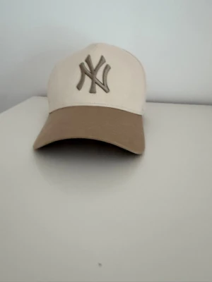 Beige NY Yankees keps - Snygg beige keps från 47 Brand med New York Yankees-logga framtill i brunt. Kepsen har böjd skärm i ljusbrun färg och klassisk sexpanelsdesign med ventilationshål. Perfekt accessoar för en avslappnad streetwear-look. Använd ca 3ggr