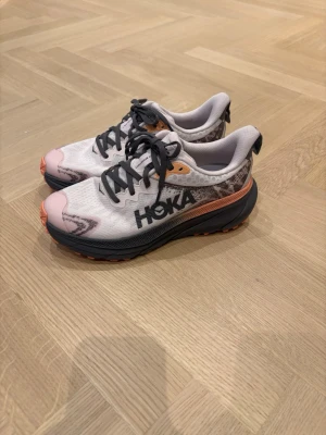 Hoka challenge ATR 7 - Snygga skor från Hoka Challenge ATR 7 . Skorna har grå/oreange sula med mönstrad undersida och mörkgrått Hoka-logga på sidan. Löpsko idealisk för både asfalt och terräng. Perfekt för löpare som söker en mångsidig sko. Helt ny med kvitto 