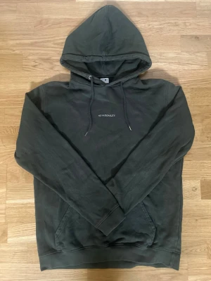 Mörkgrön NN07 Hoodie ”No Nationality” - Säljer en mörkgrön NN07 hoodie med texten 'NO NATIONALITY' tryckt på bröstet. Hoodien har klassisk huva med dragsnören och en stor magficka. Tillverkad i mjukt material och har ribbade muddar vid ärmslut och nederkant. Perfekt för en chill och avslappnad stil.