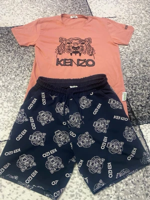 Kenzo -set med tigertryck - Snyggt -set från Kenzo med en korallfärgad t-shirt med ikoniskt tigertryck och matchande mörkblå shorts med vita Kenzo-loggor och tigerhuvuden. Perfekt för chillkvällar hemma eller ute. Mjukt och bekvämt material. Använt i gott skick.  Storlek skulle jag säga S/M men mer som S. 