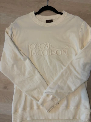 Vit sweatshirt från Oscar Jacobson - Snygg vit sweatshirt från Oscar Jacobson med broderad logga framtill. Tröjan har rund halsringning, långa ärmar och ribbade muddar vid ärmslut och nederkant. Perfekt för en clean och stilren look.