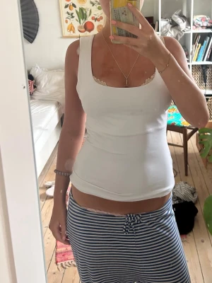 Vit ribbad linnetopp - Säljer en enkel och stilren vit ribbad linnetopp med breda axelband och rundad urringning. Toppen är ärmlös och har en tight passform som sitter snyggt på kroppen. Perfekt att matcha med jeans eller kjol för en clean look.