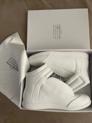Vita Maison Margiela high top sneakers - Säljer one of a kind Masion margiela skor i storlek 43 De är perfekt att ha på sig till sommaren, passar perfekt till dig som vill ha unika skor 😉 hör av mig vid frågor vet ja 😀